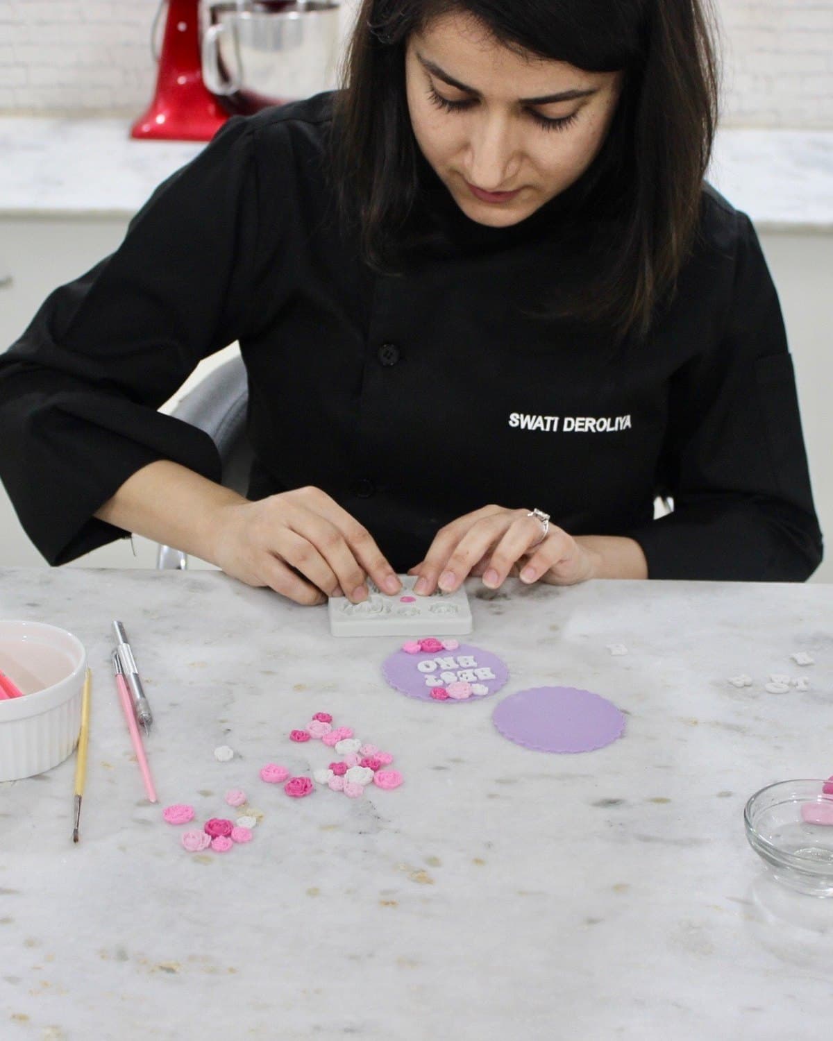 Swati Deroliya in her chef's jacket at the marble bench, shaping handmade sugar flowers