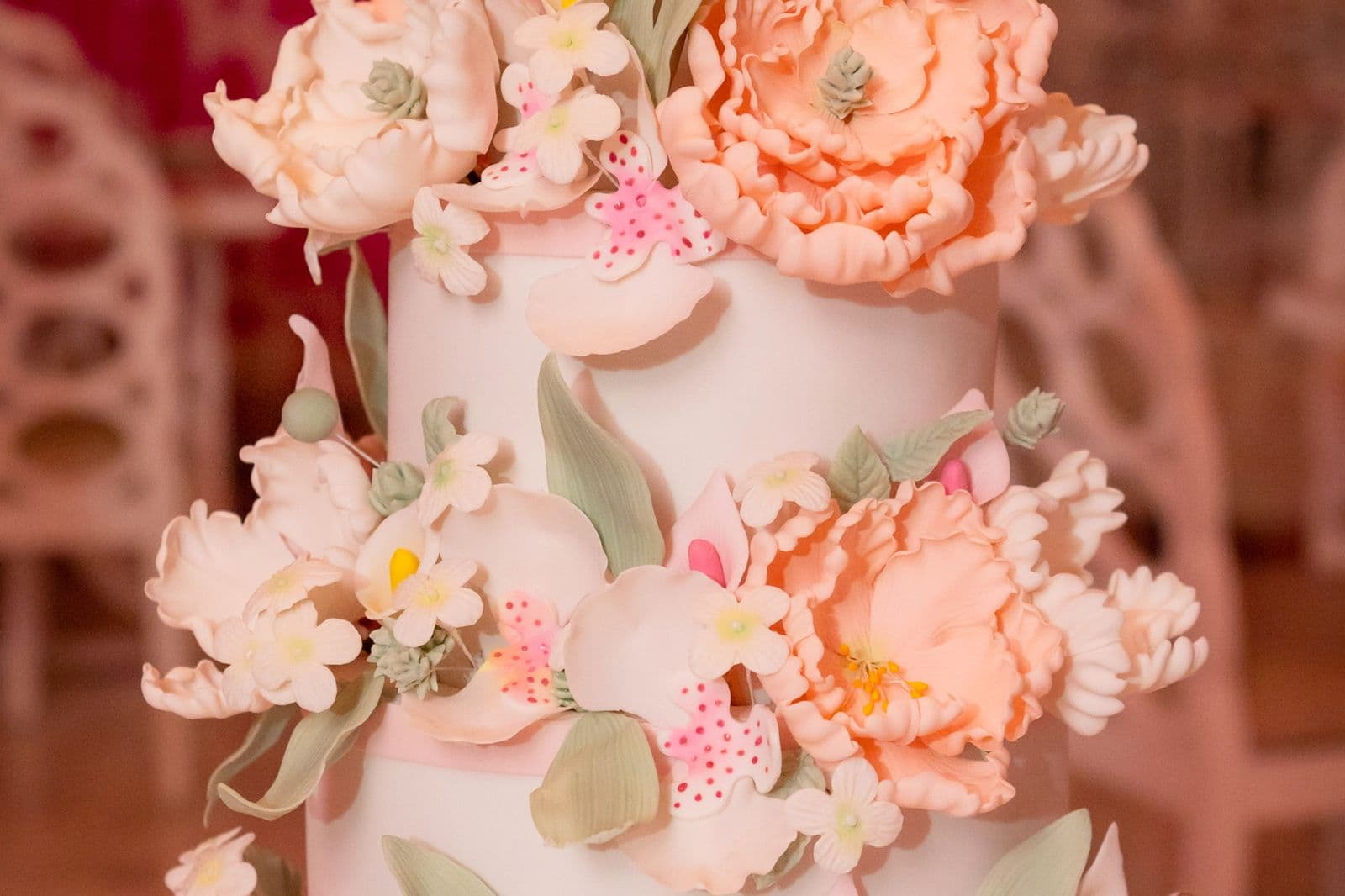 Close-up of handmade blush sugar peonies and blossom on a tiered cake